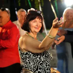 Uśmiechnięta kobieta w panterce tańczy na imprezie. W tle widać bawiących się ludzi, nie ma mocnych obsada, tylko radość.