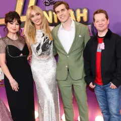 Hannah Montana obsada świętuje 20. rocznicę serialu. Gwiazdy w olśniewających strojach pozują na fioletowym dywanie.