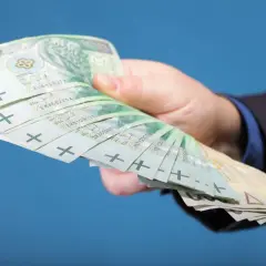 Dłoń w garniturze trzyma plik banknotów 100 zł. Zastanawiasz się, ile zarabiają gwiazdy seriali?