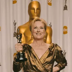 Meryl Streep z Oscarem, aktorka, która zdobyła najwięcej oscarów w XXI wieku, pozuje na tle złotych statuetek.