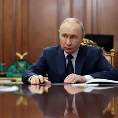 Władimir Putin siedzi przy biurku, zamyślony. Za nim rosyjskie flagi. Czeka na nas świat.