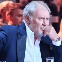 Andrzej Grabowski żyje, siedzi w eleganckim garniturze, zamyślony, z dłonią przy ustach. W tle widać innych ludzi.