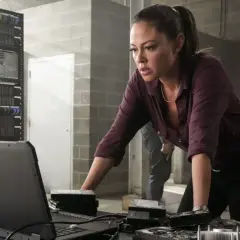 NCIS Hawaii obsada: Jane Tennant analizuje dane na laptopie, otoczona serwerami i dyskami twardymi.