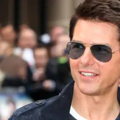 Tom Cruise w okularach przeciwsłonecznych, uśmiechnięty, na tle tłumu. Wygląda jakby właśnie świętował swoje urodziny, kiedy urodził się Tom Cruise.