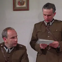Dwóch mężczyzn w mundurach wojskowych, jeden czyta dokument. Scena z filmu "Pogranicze w ogniu obsada".