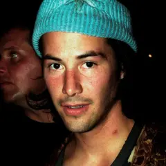 Młody Keanu Reeves w niebieskiej czapce, obok niego inny mężczyzna. Trudno zgadnąć, ile lat ma Keanu Reeves na tym zdjęciu.