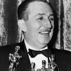 Walt Disney, który zdobył najwięcej Oscarów, uśmiecha się, trzymając statuetki.
