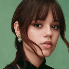 Jenna Ortega z kolczykami w kształcie gwiazdek. Jej włosy są ciemnobrązowe, a tło zielone.