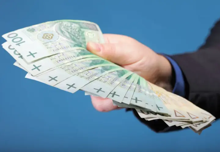 Dłoń w garniturze trzyma plik banknotów 100 zł. Zastanawiasz się, ile zarabiają gwiazdy seriali?