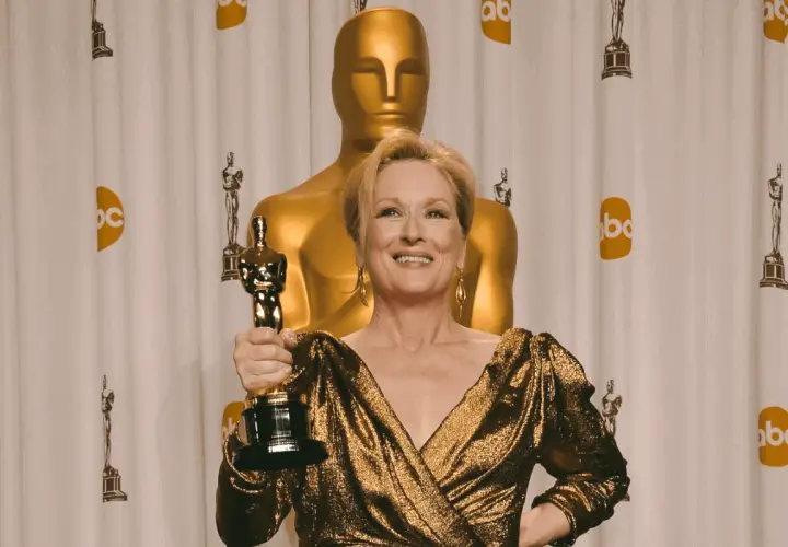 Meryl Streep z Oscarem, aktorka, która zdobyła najwięcej oscarów w XXI wieku, pozuje na tle złotych statuetek.