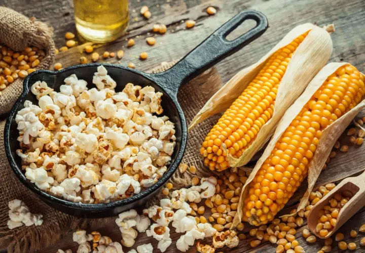 Pachnący, świeży popcorn w żeliwnej patelni, obok kolb kukurydzy i ziaren. Zastanawiasz się, ile kosztuje duży popcorn w Heliosie?