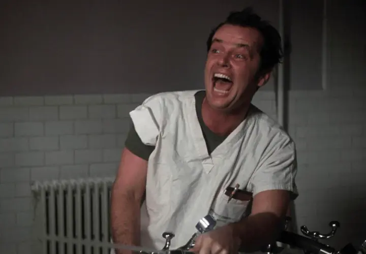 Jack Nicholson w roli McMurphy'ego w "Locie nad kukułczym gniazdem" obsada, szaleńczo krzyczy w szpitalnym ubraniu.