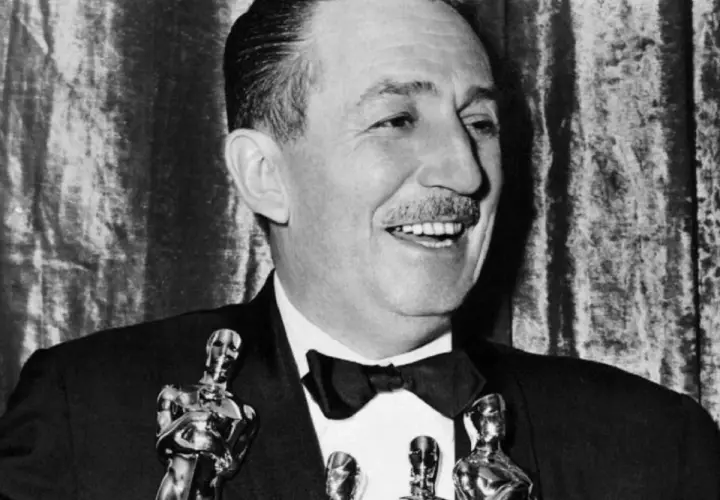 Walt Disney, który zdobył najwięcej Oscarów, uśmiecha się, trzymając statuetki.