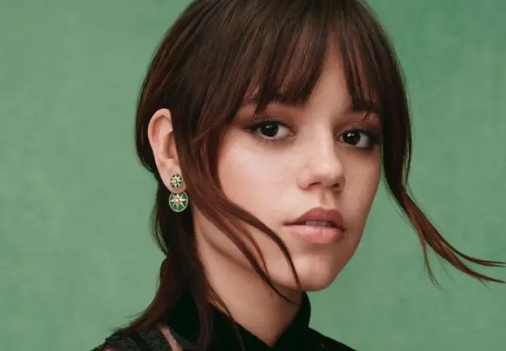 Jenna Ortega z kolczykami w kształcie gwiazdek. Jej włosy są ciemnobrązowe, a tło zielone.