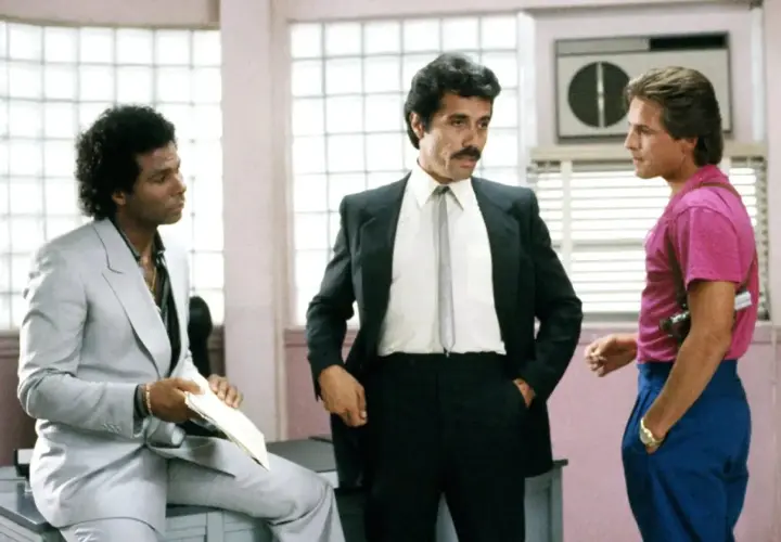Trzech mężczyzn, w tym policjanci z Miami obsada, w tym Sonny Crockett i Ricardo Tubbs, rozmawiają w biurze.