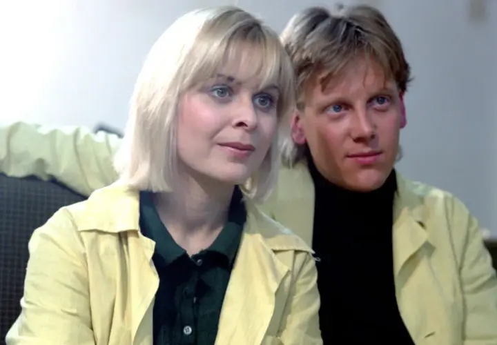 W labiryncie obsada: blondynka i blondyn w żółtych płaszczach, siedzą obok siebie.