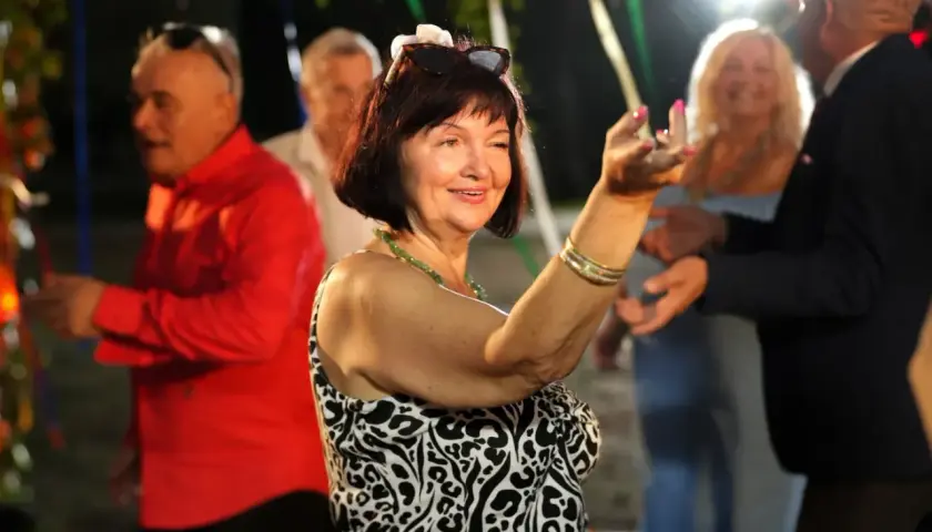 Uśmiechnięta kobieta w panterce tańczy na imprezie. W tle widać bawiących się ludzi, nie ma mocnych obsada, tylko radość.