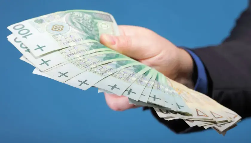 Dłoń w garniturze trzyma plik banknotów 100 zł. Zastanawiasz się, ile zarabiają gwiazdy seriali?