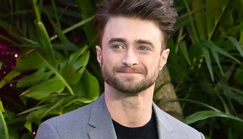 Daniel Radcliffe, który grał Harry'ego Pottera, w szarym garniturze na tle zieleni.