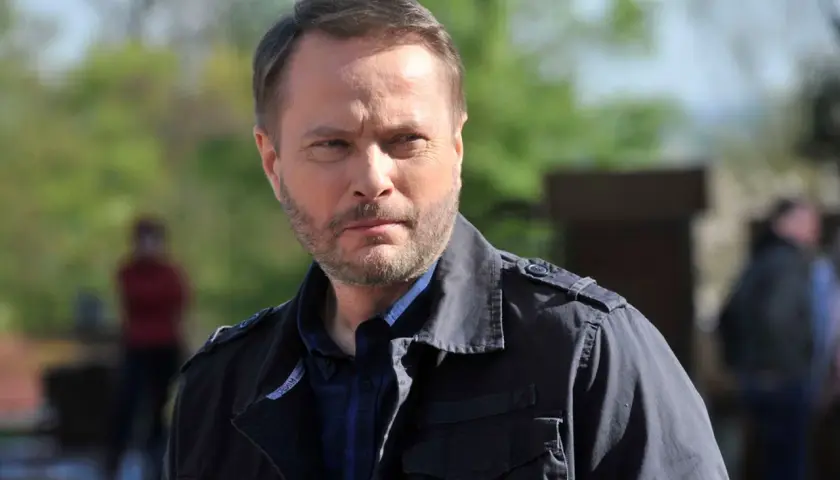 Artur Żmijewski, który gra Ojca Mateusza, w ciemnej kurtce i kratowanej koszuli, zamyślony.