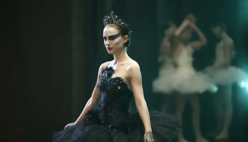 Natalie Portman jako Czarny Łabędź w koronie i czarnej tutu, z innymi tancerkami w tle.
