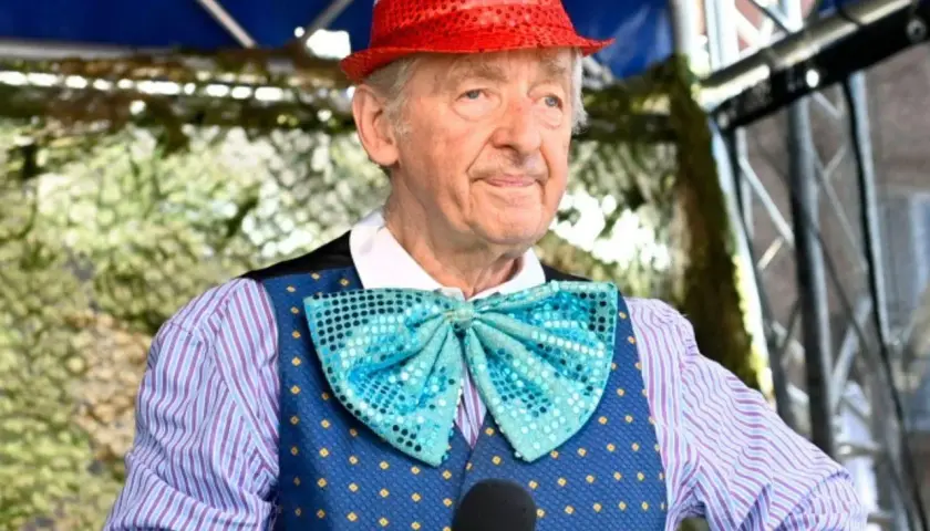 Uśmiechnięty Andrzej Rosiewicz w cekinowym kapeluszu i muszce, trzymający mikrofon. Wiek artysty to 80 lat.