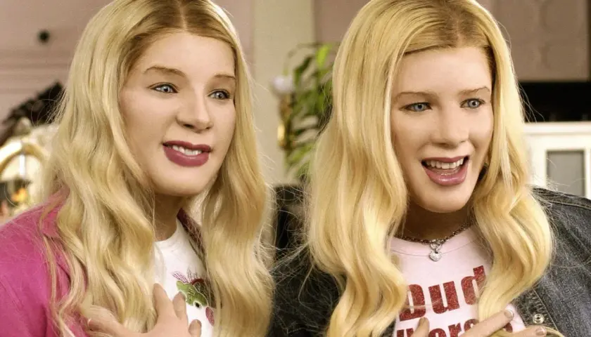 Dwie blondynki w perukach, przypominające bohaterki z filmu "Agenci bardzo specjalni obsada", śmieją się z rękami na piersi.