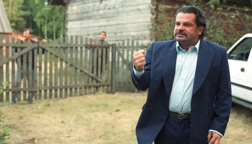 Mężczyzna w garniturze, jakby z filmu "To ja, złodziej", pokazuje pięść. Za nim przez płot wyglądają inni.