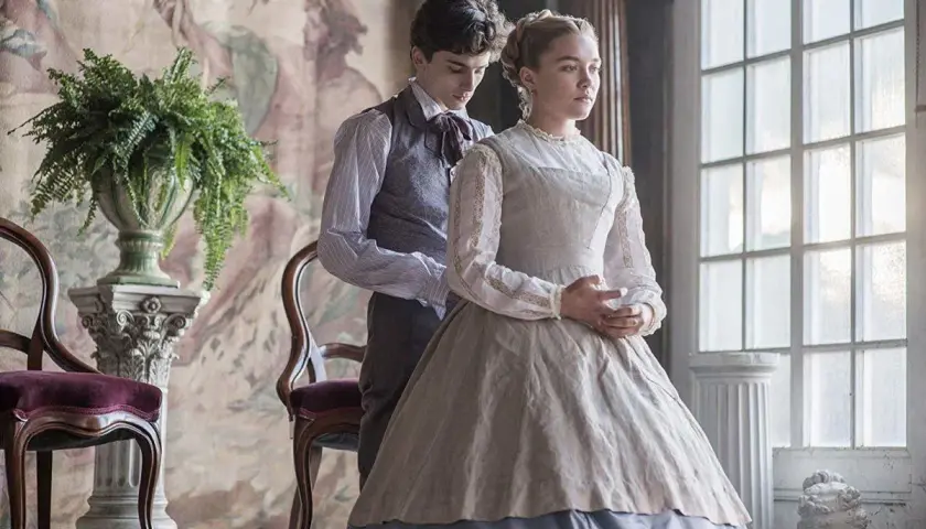 Małe kobietki obsada: Timothée Chalamet i Florence Pugh w strojach z epoki, w eleganckim wnętrzu.