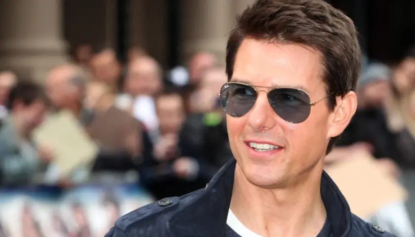 Tom Cruise w okularach przeciwsłonecznych, uśmiechnięty, na tle tłumu. Wygląda jakby właśnie świętował swoje urodziny, kiedy urodził się Tom Cruise.