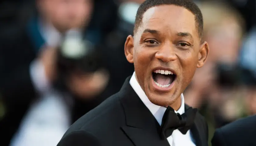 Will Smith w czarnym smokingu z muszką, uśmiecha się szeroko. Ciekawe, ile lat ma Will Smith, patrząc na jego energię!