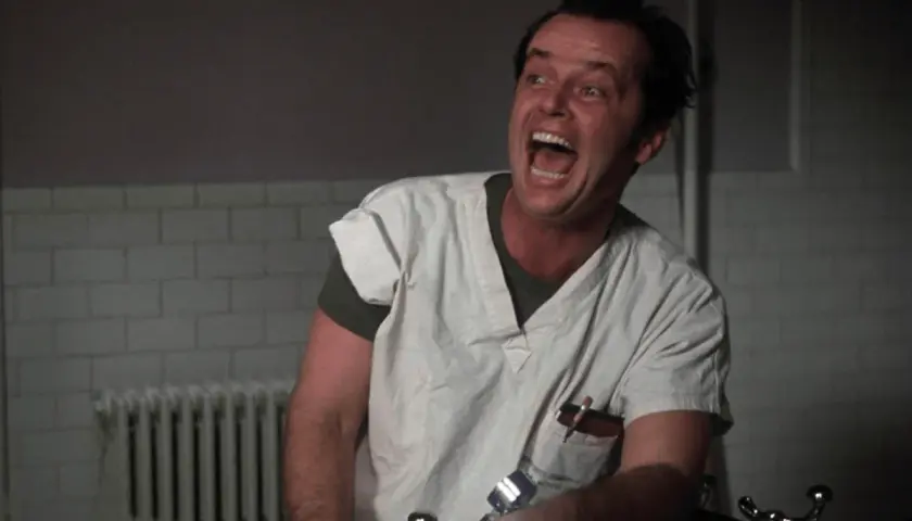 Jack Nicholson w roli McMurphy'ego w "Locie nad kukułczym gniazdem" obsada, szaleńczo krzyczy w szpitalnym ubraniu.