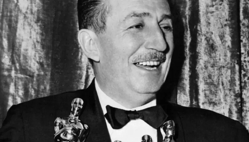 Walt Disney, który zdobył najwięcej Oscarów, uśmiecha się, trzymając statuetki.