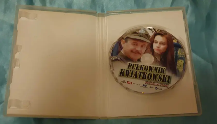 Płyta DVD z filmem "Pułkownik Kwiatkowski" i jego obsadą. Widoczni są główni bohaterowie, pułkownik i młoda kobieta.