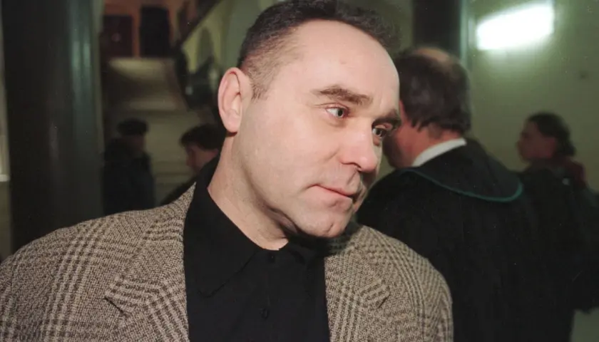Mężczyzna w tweedowej marynarce, jak zostałem gangsterem o kim, w tle prawnik w todze.