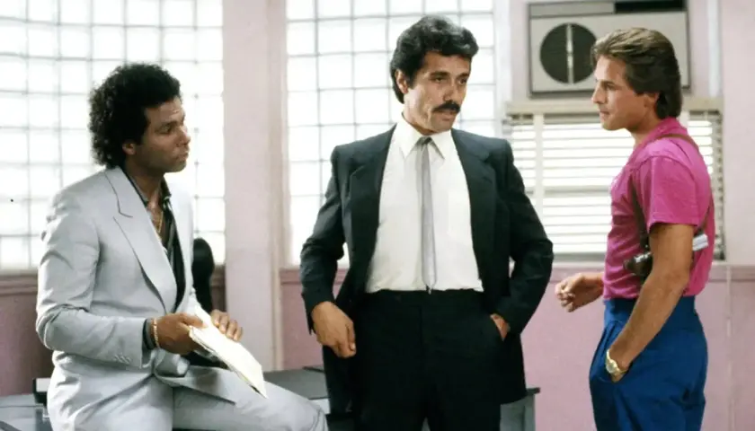 Trzech mężczyzn, w tym policjanci z Miami obsada, w tym Sonny Crockett i Ricardo Tubbs, rozmawiają w biurze.