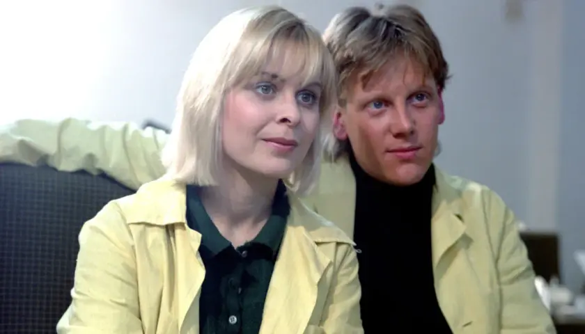 W labiryncie obsada: blondynka i blondyn w żółtych płaszczach, siedzą obok siebie.