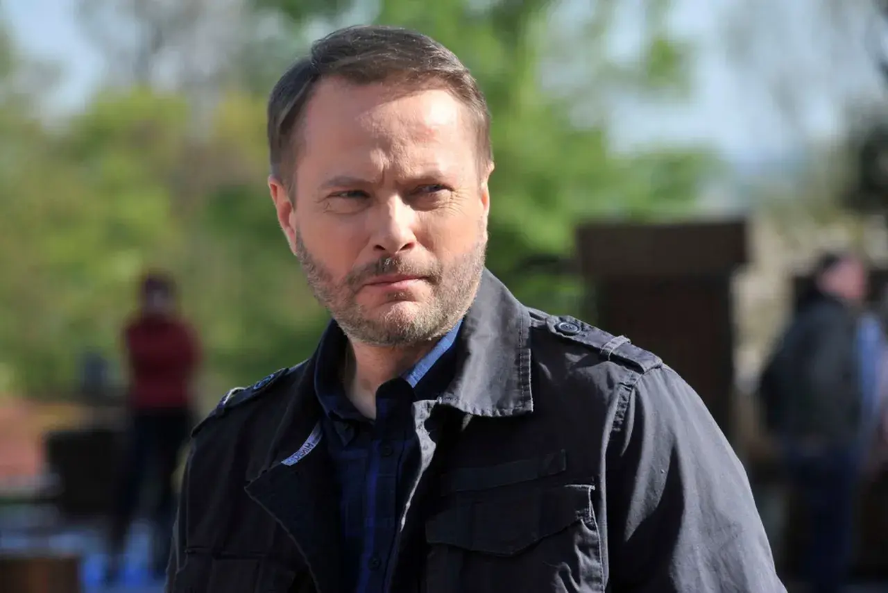 Artur Żmijewski, który gra Ojca Mateusza, w ciemnej kurtce i kratowanej koszuli, zamyślony.