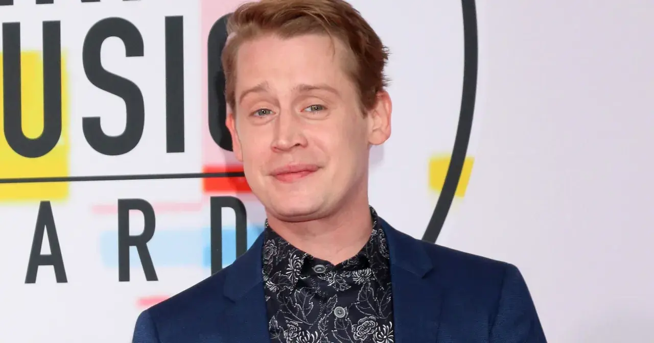Macaulay Culkin, żyje i ma się dobrze, pozuje na tle napisu "MUSIC AWARDS".