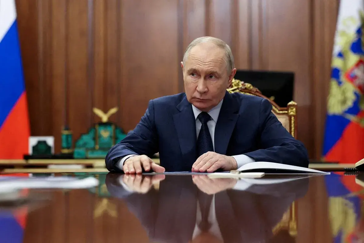 Władimir Putin siedzi przy biurku, zamyślony. Za nim rosyjskie flagi. Czeka na nas świat.