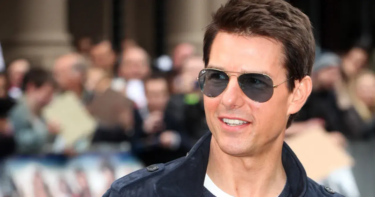 Tom Cruise w okularach przeciwsłonecznych, uśmiechnięty, na tle tłumu. Wygląda jakby właśnie świętował swoje urodziny, kiedy urodził się Tom Cruise.