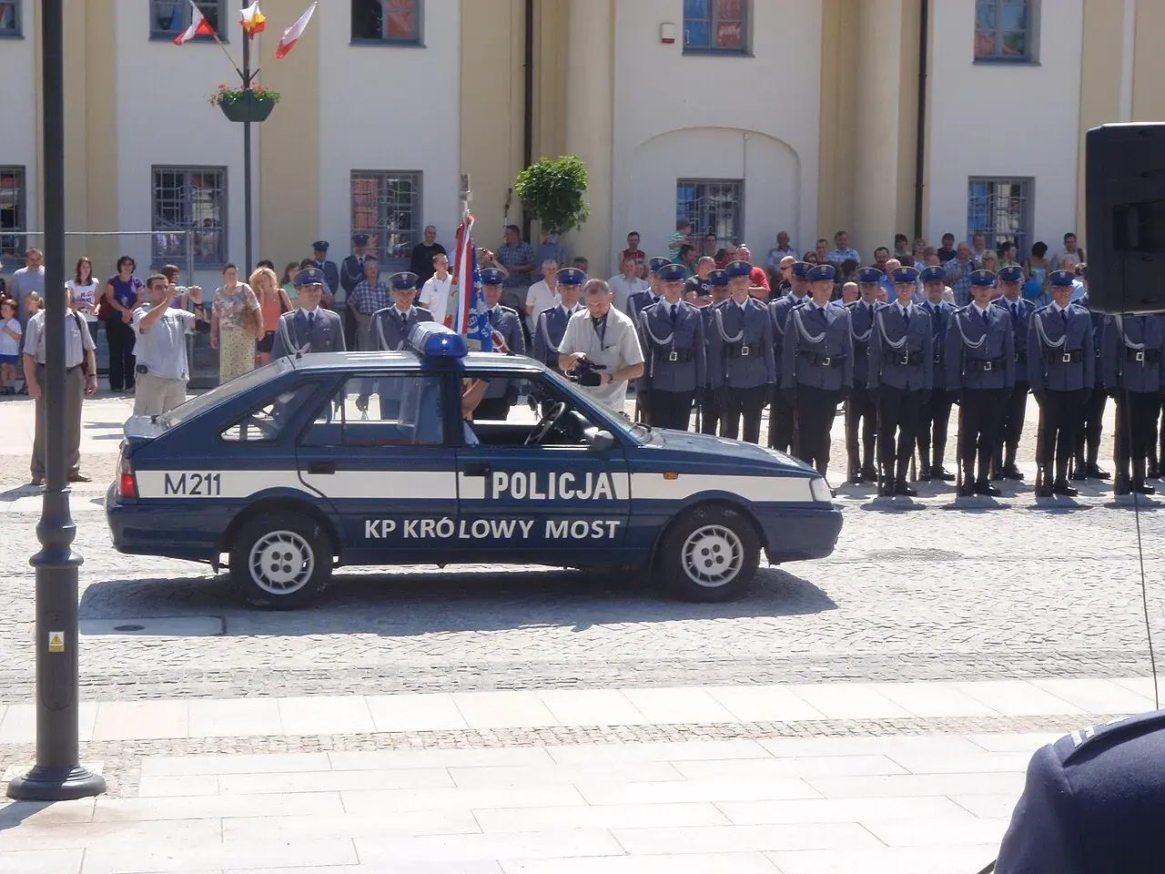 U pana Boga w ogródku obsada: policjanci w mundurach stoją w szeregu obok radiowozu.