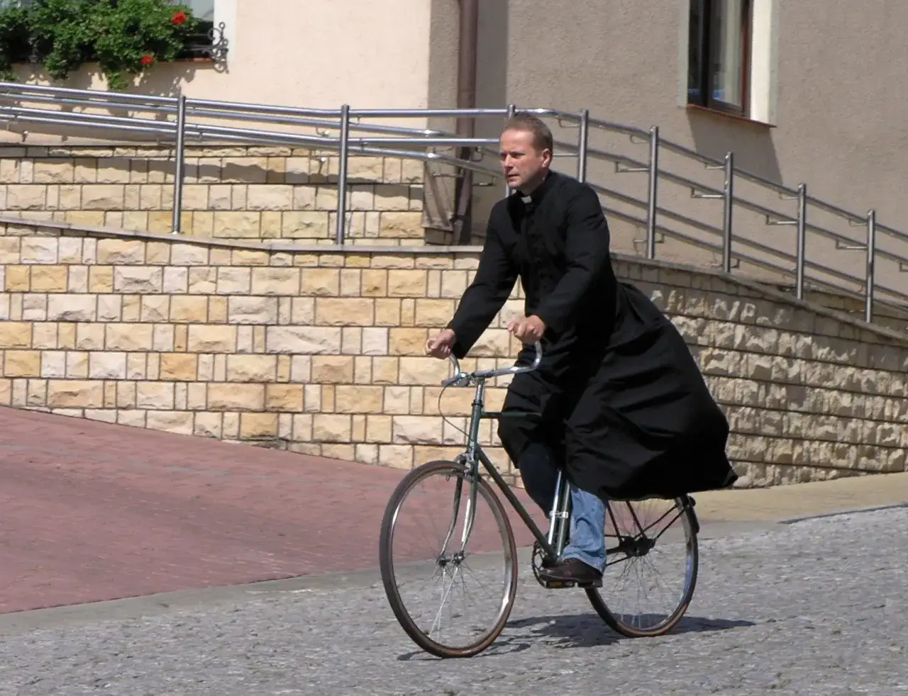 Kto gra Ojca Mateusza? Aktor w sutannie pędzi rowerem po bruku, wiatr rozwiewa jego szaty.