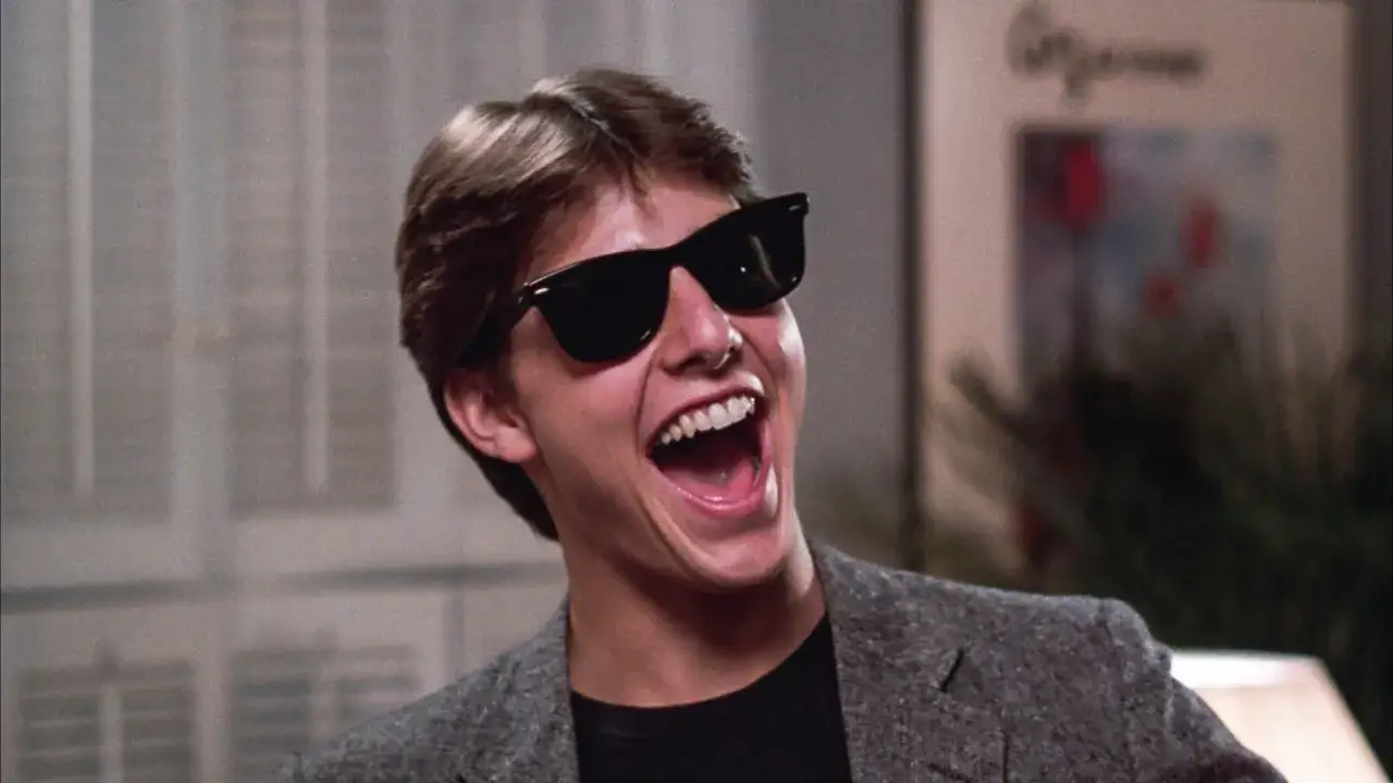 Młody Tom Cruise w okularach przeciwsłonecznych śmieje się głośno. Wygląda jakby właśnie dowiedział się, kiedy urodził się Tom Cruise.