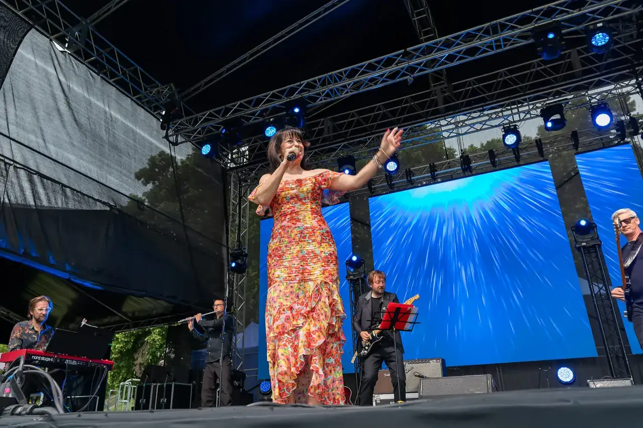 Krystyna Giżowska w kwiecistej sukni śpiewa na scenie, otoczona muzykami. Ile lat ma Krystyna Giżowska? Tego nie widać, ale energia na scenie jest!