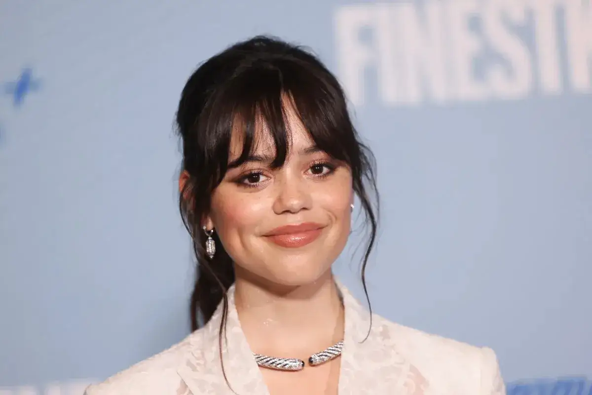 Jenna Ortega, uśmiechnięta, w białej koronkowej marynarce i błyszczącym naszyjniku. Ciekawe, ile lat ma Jenna Ortega w 2025 roku?
