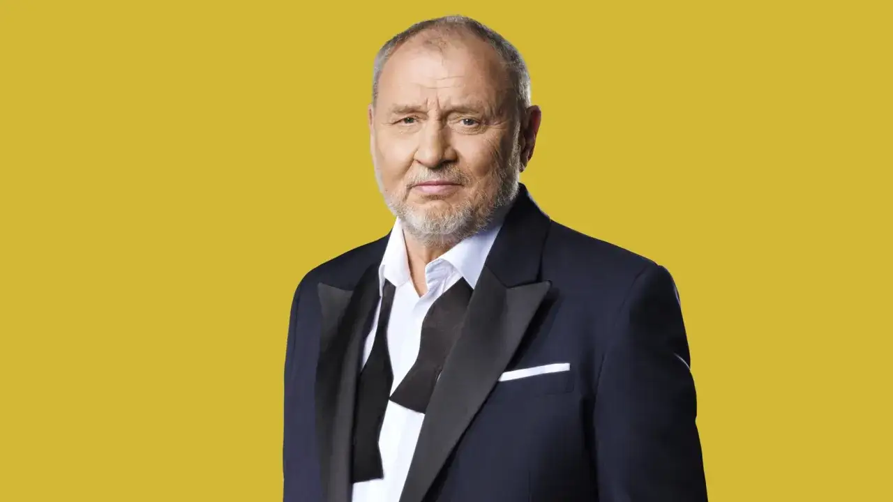 Andrzej Grabowski żyje, wygląda świetnie w garniturze i z rozluźnioną muszką na tle żółtej ściany.